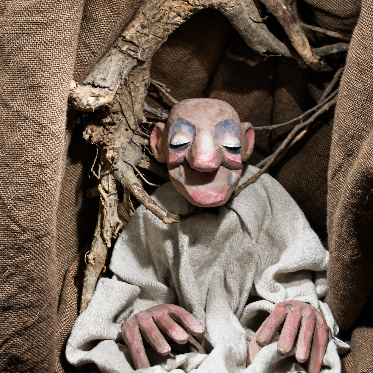 Die Puppe des Alten mit geschlossenen Augen zwischen Wurzeln und grobem Stoff